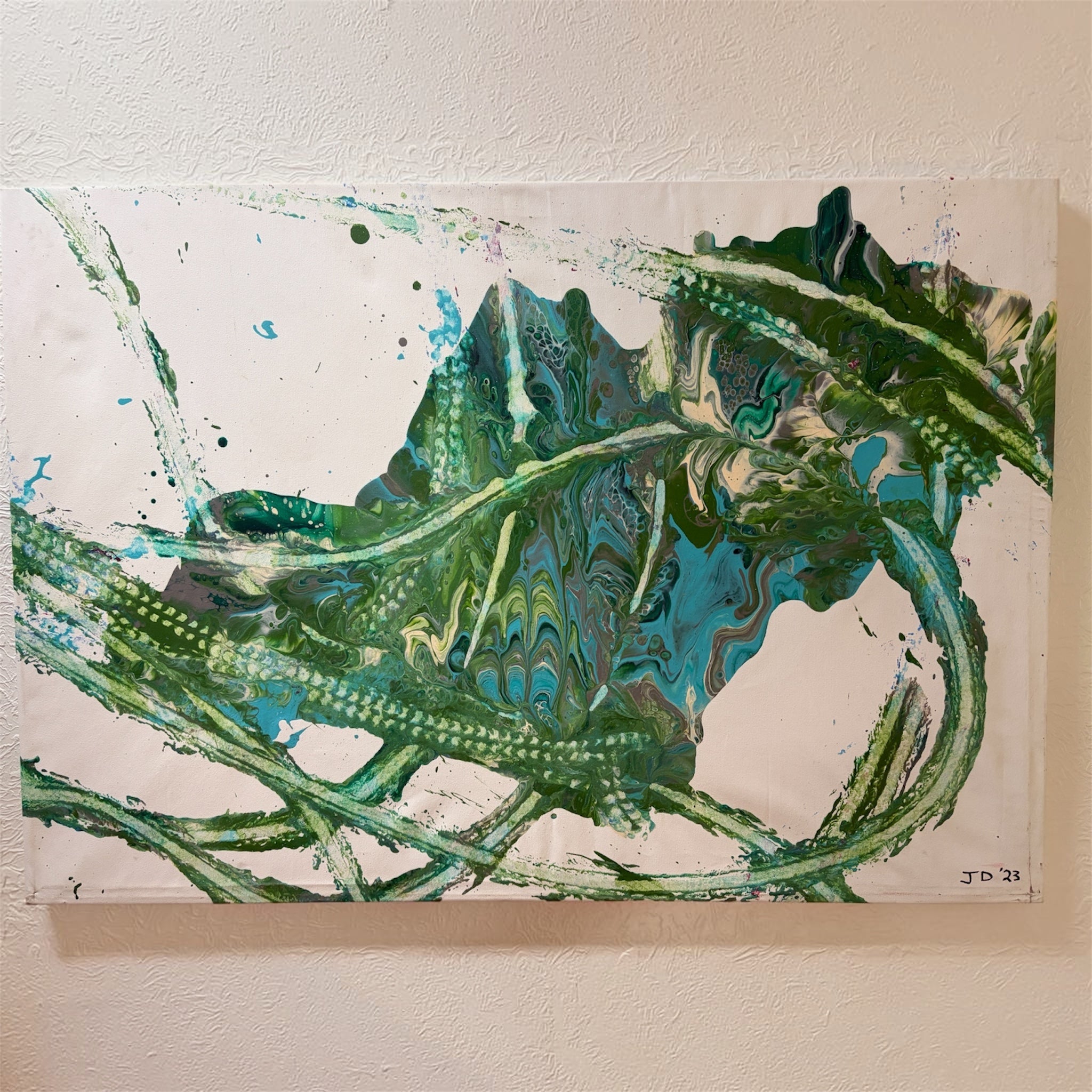 An abstract fluid acrylic painting featuring swirling patterns of green, teal, and black paint on a white background, mounted on a textured beige wall.